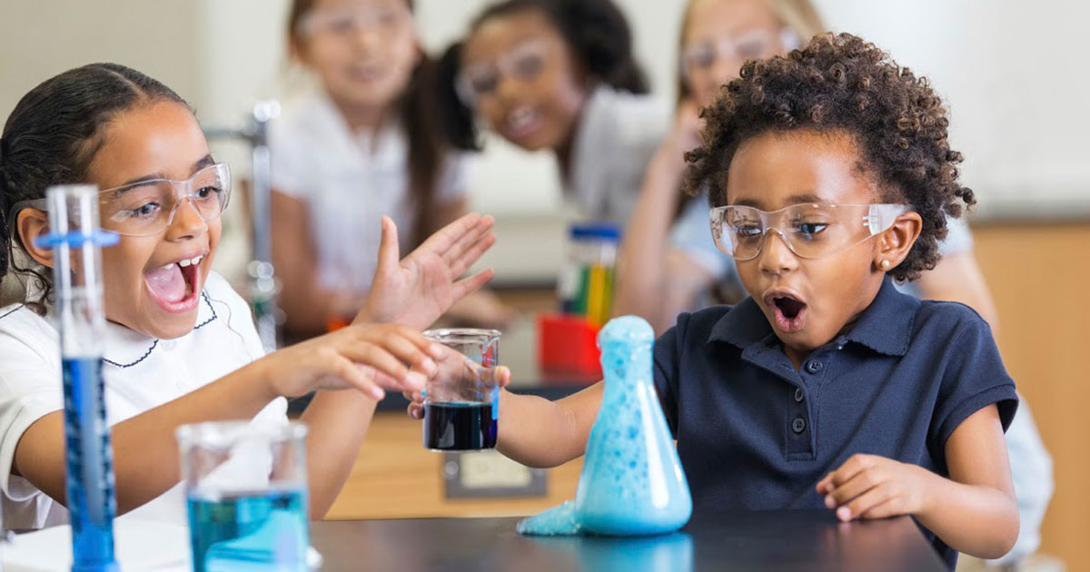 Two kids in a classroom doing a scientific experiment with blue liquid.